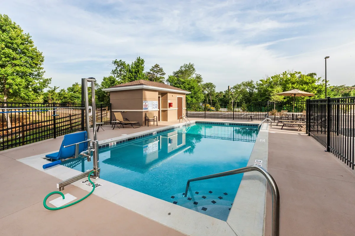 This image features a vibrant outdoor swimming pool surrounded by poolside lounge chairs and a pool house. The scene is lively, with hints of social activity such as children playing and guests sunbathing. The warm, inviting atmosphere suggests summer fun and relaxation.