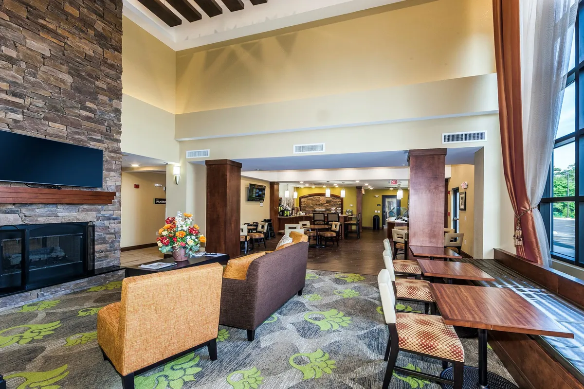 This image provides a view of a cozy seating area arranged around a stone fireplace, with large windows letting in natural light and decorative flowers adding warmth. While not a bedroom or living room per se, it presents a universally inviting, accessible space within the property, suggesting thoughtful touches and a welcoming atmosphere for relaxation.