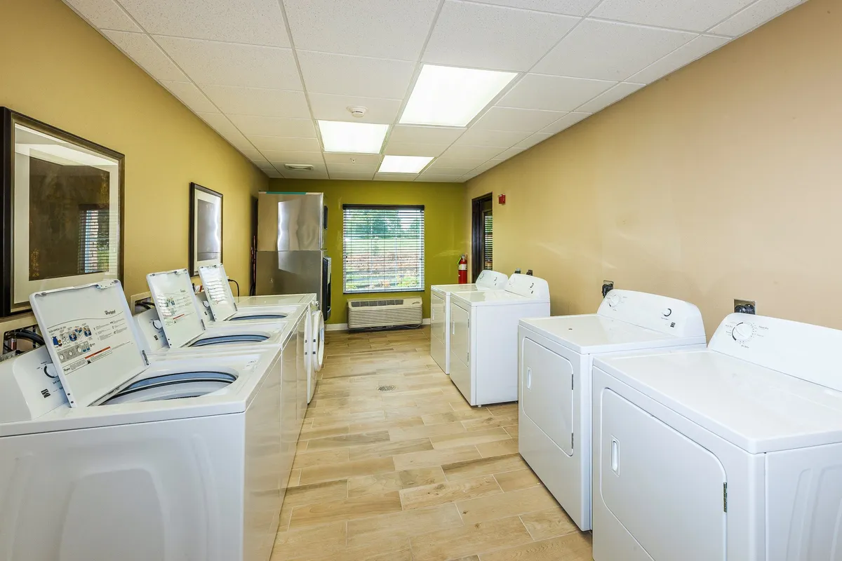 This scene features a tidy, organized guest laundry room with washing machines, dryers, and large windows that let in natural light. The practical design ensures guests experience all the comforts of home even during extended stays.