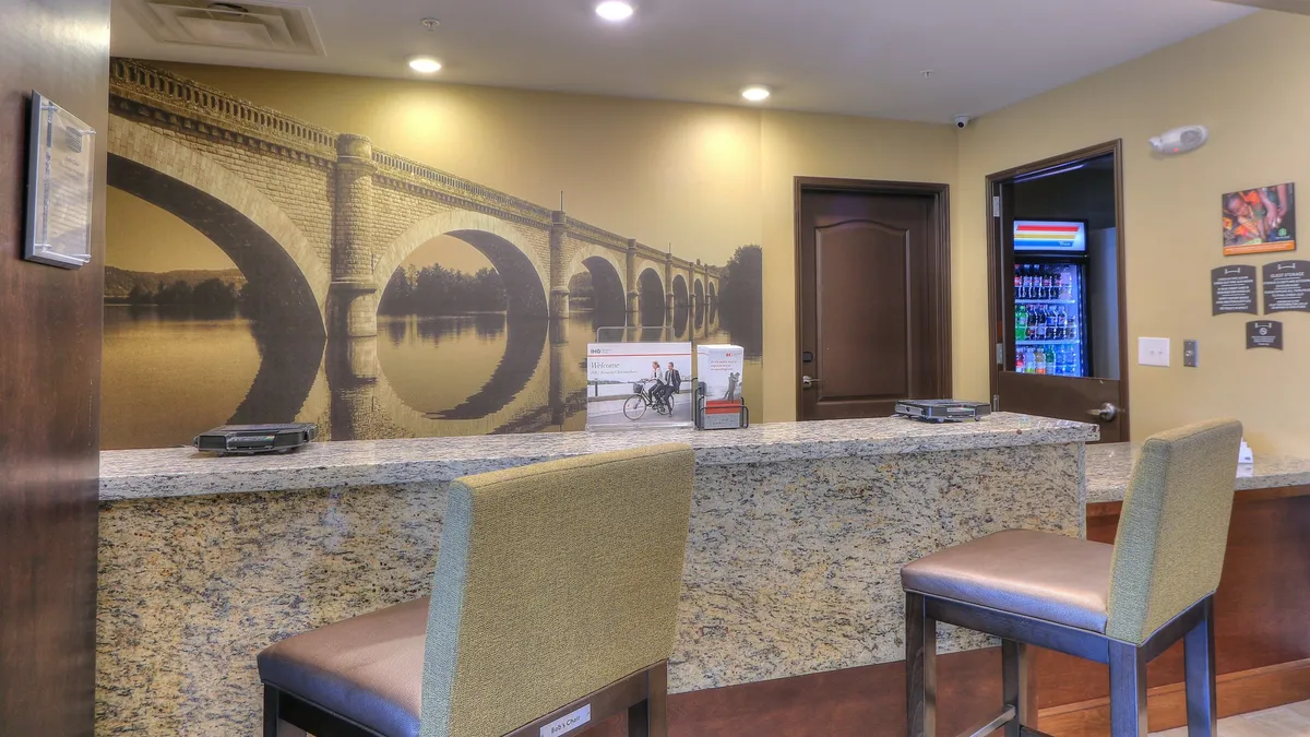 This image captures the hotel's welcoming reception area, featuring a distinctive bridge mural, comfortable seating, and a bright, inviting atmosphere. The lobby space is open and hints at a smooth guest arrival experience, while the mural subtly references the local landscape and potential for nearby exploration.