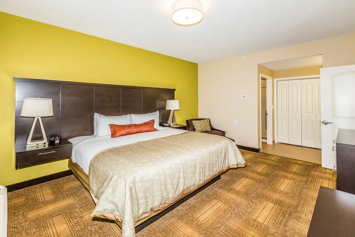 This image features a comfortable bedroom setup with a plush bed, accent wall, lamps, and a cozy seating area. The soft lighting and inviting decor create an atmosphere of relaxation and tranquility, emphasizing the restful qualities of the suite. The spacious layout and thoughtful touches are evident, supporting the idea of a serene private retreat.