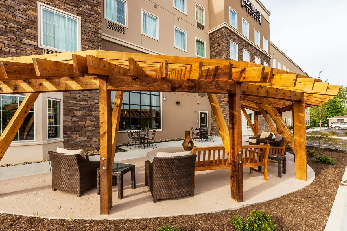 The image showcases an outdoor area with a wooden pergola, comfortable seating, and decorative touches. The environment is designed for relaxation and social gatherings, perfect for grilling or enjoying an evening outdoors.